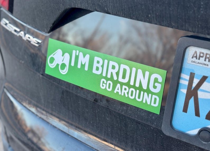 Op de afbeelding: Groene en witte auto sticker met een verrekijker en de tekst "I'm Birding Go Around".