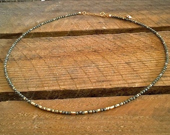 May include: A delicate gold and black necklace made of small beads. The necklace is on a wooden surface.