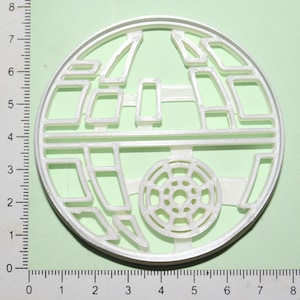 May include: White plastic cookie cutter shaped like the Death Star from Star Wars. The cutter is approximately 7 cm in diameter.