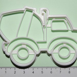 May include: White plastic cookie cutter shaped like a cement mixer truck. The cutter is approximately 7.5 cm long and 5 cm wide.