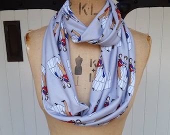 May include: A light gray infinity scarf with a repeating pattern of women in white dresses and men in red and blue uniforms. The women are holding hands and dancing.