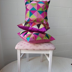 Peut inclure: Un ensemble de trois coussins géométriques colorés sur une chaise blanche avec un siège à motif floral rose.