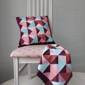 Peut inclure: Une chaise blanche avec un siège à motif floral rose et un coussin bordeaux avec un motif géométrique de triangles roses, bruns et turquoise. Le coussin est posé sur la chaise et une jetée assortie est drapée sur le dossier de la chaise.