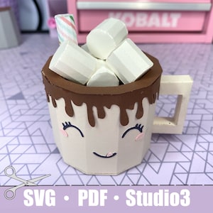 a tan mug with a smiling face on it. There is chocolate dripping over the top edge. There are also paper marshmallows sitting inside the mug with a stir stick. The bottom shows that it is a SVG, PDG, and Studio3 file.