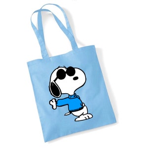 K&ouml;nnte beinhalten: Eine hellblaue Tragetasche mit einem Cartoon-Bild von Snoopy, der eine Sonnenbrille und einen blauen Pullover tr&auml;gt. Snoopy schaut nach rechts und hat seinen rechten Arm ausgestreckt.
