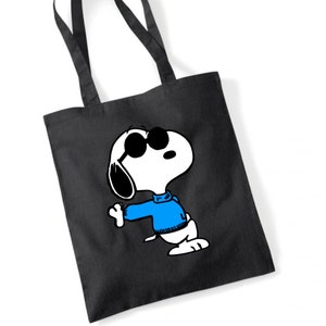 K&ouml;nnte beinhalten: Eine schwarze Tragetasche mit einem wei&szlig;en Cartoon-Bild von Snoopy, der eine Sonnenbrille und einen blauen Pullover tr&auml;gt.