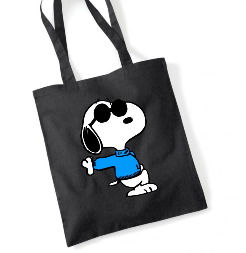 K&ouml;nnte beinhalten: Eine schwarze Tragetasche mit einem wei&szlig;en Cartoon-Bild von Snoopy, der eine Sonnenbrille und einen blauen Pullover tr&auml;gt.