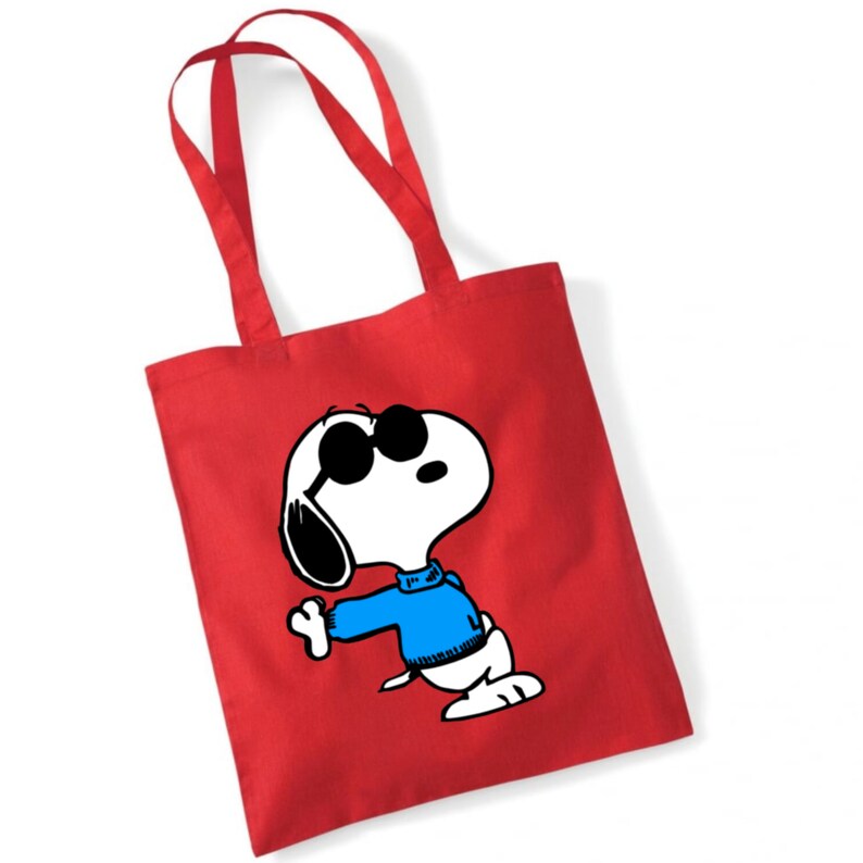 K&ouml;nnte beinhalten: Rote Stofftasche mit einem wei&szlig;en Comic-Hund, der eine Sonnenbrille und einen blauen Pullover tr&auml;gt. Der Hund schaut nach oben und hat die Zunge herausgestreckt.
