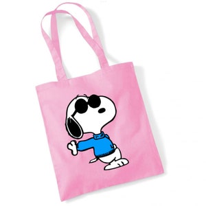 K&ouml;nnte beinhalten: Rosa Canvas-Tragetasche mit einem Cartoon-Bild von Snoopy, der eine Sonnenbrille und einen blauen Pullover tr&auml;gt.