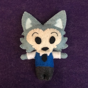 May include: A gray and white felt plush toy of a wolf wearing a blue vest and a black tie. The wolf has a white shirt and gray pants.