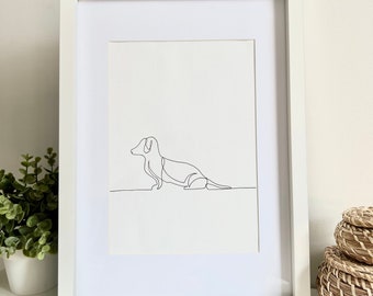 May include: A white framed print of a line drawing of a dachshund dog. The dog is sitting with its head turned to the left.