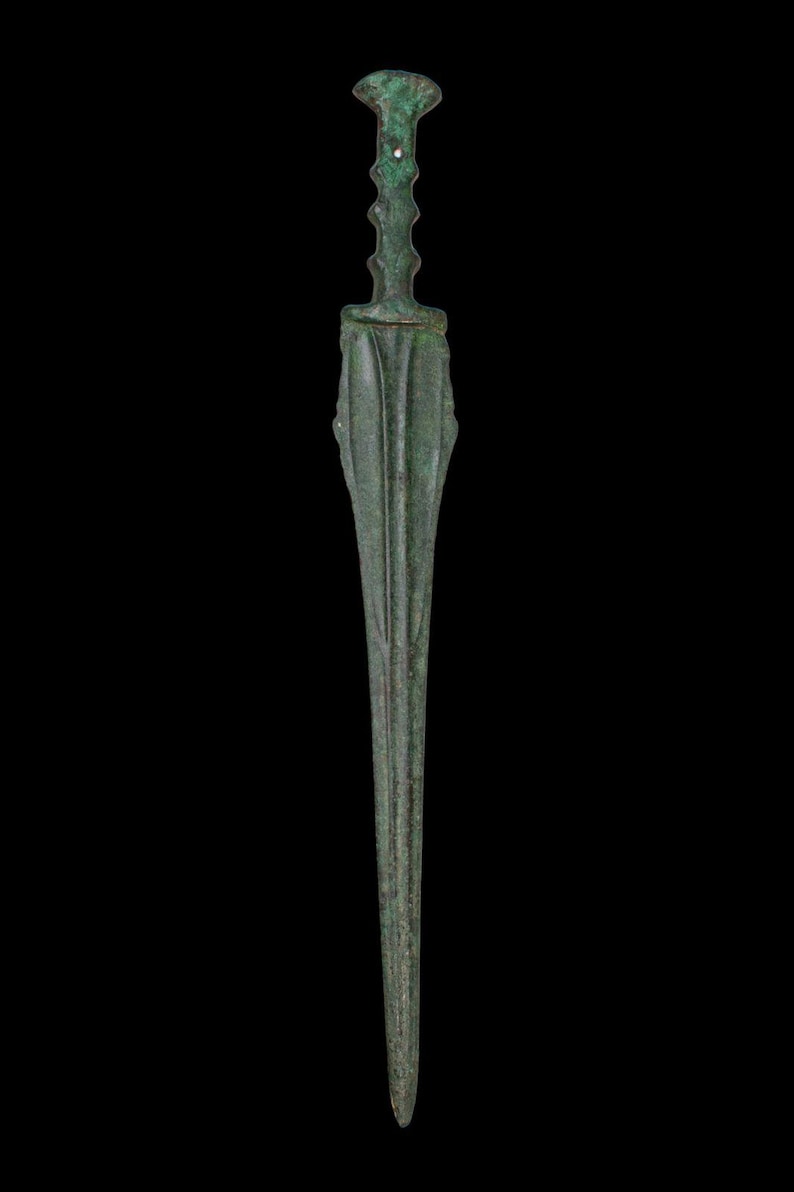 May include: A bronze dagger with a long, slender blade and a detailed handle. The handle features a series of ridges and a flared base. The dagger has a dark green patina, suggesting age. The background is solid black.