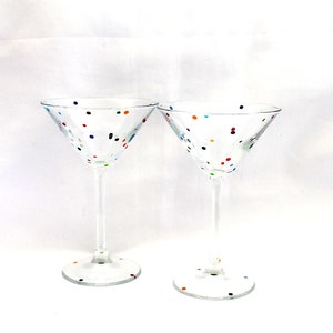 Puede incluir: Dos copas de martini de vidrio transparente con lunares de colores. Las copas están vacías y tienen un tallo y una copa ancha.