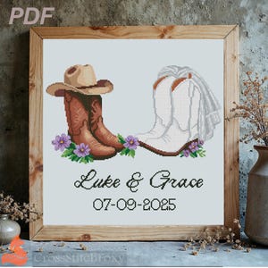 May include: Cross-stitch artwork in a wooden frame depicting a cowboy hat and boots. The boots are brown and white, with purple flowers. Text reads "Luke & Grace" and "07-09-2025".
