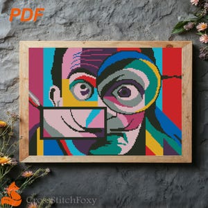 May include: A framed cross-stitch portrait with a colorful, geometric design. The artwork features a stylized face with a magnifying glass, rendered in shades of blue, red, yellow, and pink. The text "PDF" is in the upper left corner.