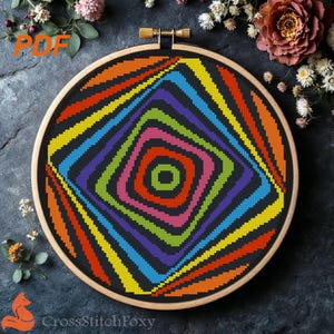 May include: A colorful cross-stitch pattern in a wooden embroidery hoop. The design features a central square with concentric squares in vibrant colors: red, pink, green, yellow, and blue. The text "PDF" is in the upper left corner, and "CrossStitchFoxy" is at the bottom.