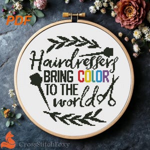 以下が含まれることがあります： 「Hairdressers Bring COLOR to the world」の文字が入ったクロスステッチ刺繍枠。 「COLOR」の文字は虹色です。 デザインには、櫛、ハサミ、葉のアクセントが含まれています。