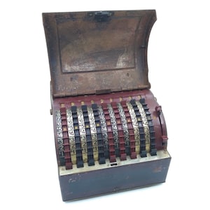 May include: A vintage, red and black, metal adding machine with a hinged lid. The machine has multiple rows of numbered dials with a crank on the right side.