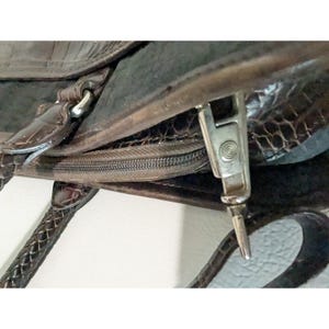 May include: Close-up of a brown leather handbag with a zipper closure and a silver zipper pull. The bag has a braided handle.