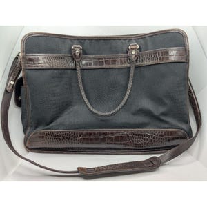 May include: A black canvas briefcase with brown leather trim and a crocodile embossed design. The bag has a top handle and a shoulder strap.