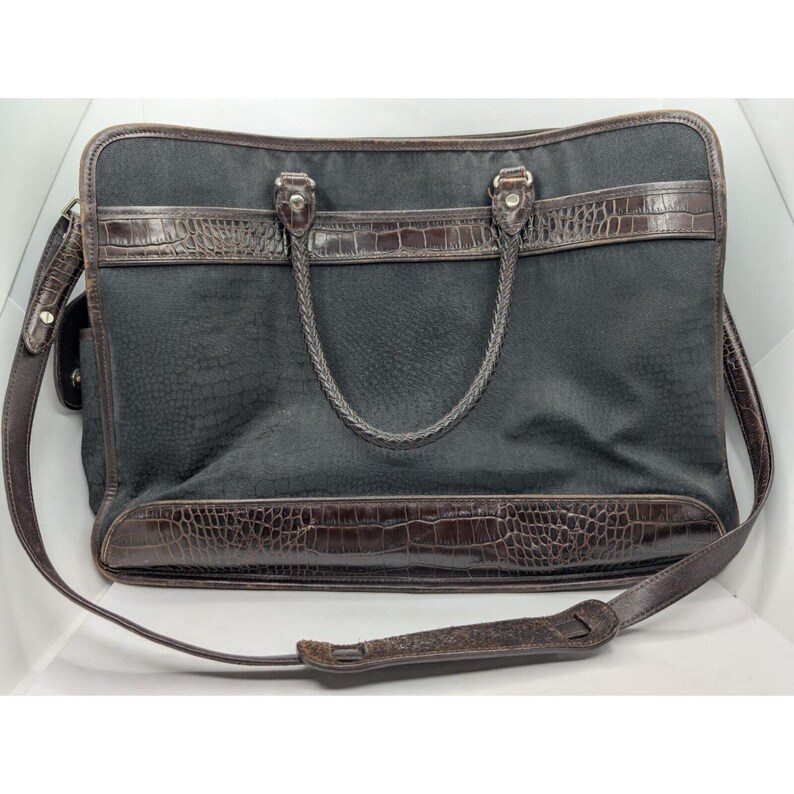 May include: A black canvas briefcase with brown leather trim and a crocodile embossed design. The bag has a top handle and a shoulder strap.