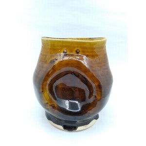 May include: A brown ceramic mug with a unique, rounded shape and a glossy glaze. The mug has a slightly uneven base and a wide, rounded opening.