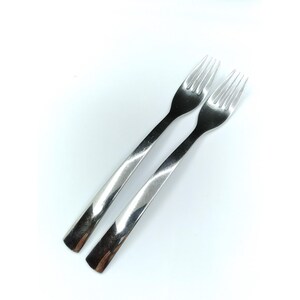 May include: Two polished stainless steel forks with a smooth, tapered handle design. Each fork features four slender tines and a reflective metallic finish, presented side-by-side against a plain white background to highlight the clean lines.