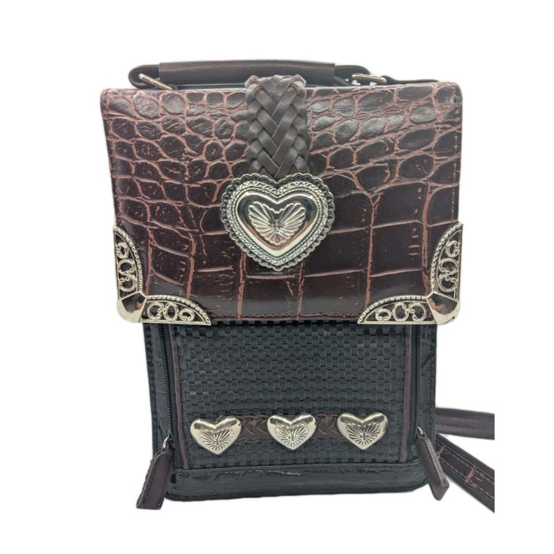 K&ouml;nnte beinhalten: Braune und schwarze Umh&auml;ngetasche mit strukturierter Kunstleder-Krokodil-Oberseite und gewebtem Boden. Die Tasche hat silberfarbene herzf&ouml;rmige Akzente und dekorative Eckst&uuml;cke. Ein geflochtener Lederriemen und Griff sind ebenfalls sichtbar.
