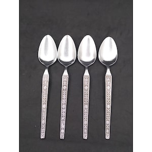 May include: Four silver spoons with oval bowls and ornate floral and geometric designs on the handles. The spoons are arranged in a row against a black background, showcasing their reflective surfaces and detailed patterns.