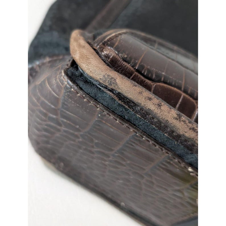May include: Close-up of a brown leather handbag with a crocodile-embossed pattern. The bag has a black suede flap and a brown leather trim.