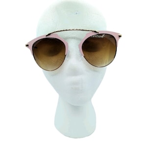 May include: Pink and gold-tone sunglasses with gradient brown lenses. The sunglasses have a double bridge design and a round frame shape. The glasses are displayed on a white mannequin head.