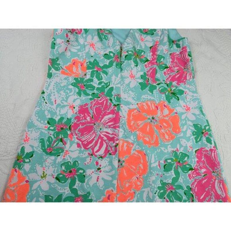 May include: A strapless dress featuring a vibrant floral pattern. The dress showcases large pink and orange flowers with green leaves against a light blue background. The dress has a zipper down the back.