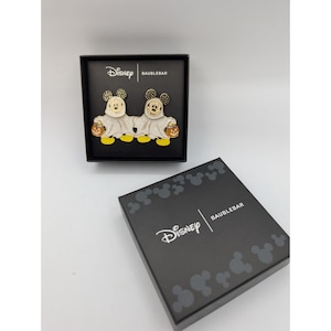 Może przedstawiać: Czarne pudełko z logo Disney i Baublebar zawiera parę kolczyków z Myszki Miki w tematyce Halloween. Kolczyki przedstawiają Myszki Miki przebrane za duchy, trzymające dynie. Widoczne jest również drugie czarne pudełko z logo Disney i Baublebar.