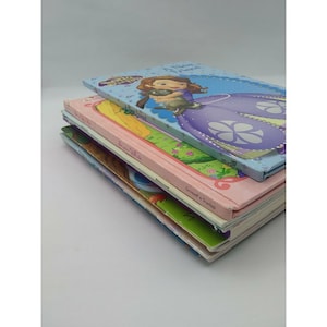 May include: A stack of four children's books featuring a princess and her animal friend. The top book is blue with a purple princess and a gray animal. The second book is pink with a white title and a green background. The third book is yellow with a blue title and a green background. The bottom book is white with a blue title and a green background.