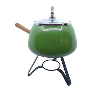May include: Green enamel fondue pot with a wooden handle and a clear glass lid. The pot sits on a black metal stand with three legs.