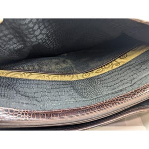 May include: The inside of a brown leather bag with a black mesh lining and a gold patterned fabric lining. The bag has a zipper closure.
