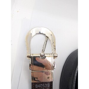 May include: Close-up of a reversible belt with a silver-colored buckle. The belt is black on one side and brown on the other. The buckle has a decorative edge. The text "B40539" is visible on the brown side of the belt.