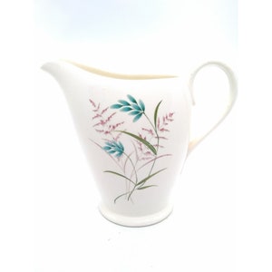 May include: White ceramic creamer with a floral design featuring pink and blue flowers and green leaves.