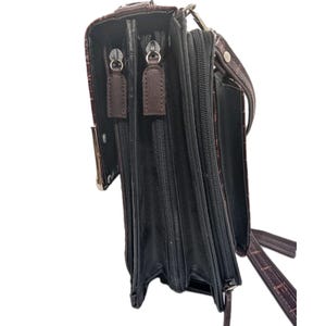 K&ouml;nnte beinhalten: Braune Leder-Umh&auml;ngetasche mit Krokodiltextur. Die Tasche hat mehrere Rei&szlig;verschlussf&auml;cher und einen langen, verstellbaren Riemen. Die Hardware ist silberfarben.