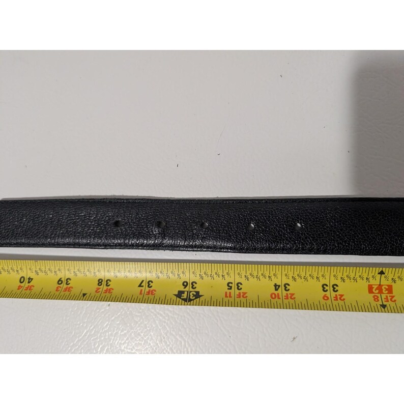 May include: A black leather belt with several evenly spaced holes. A yellow and white measuring tape is placed below the belt, showing measurements from 32 inches to 40 inches.