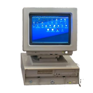 May include: A vintage beige desktop computer system featuring a bulky CRT monitor with a blue screen displaying various software icons. The base unit includes a floppy disk drive and an optical disc drive, with a small power indicator light visible.