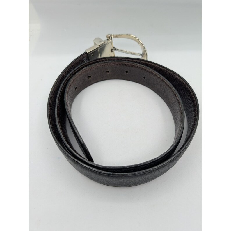 May include: A reversible belt with a silver-tone buckle. One side is black, and the other is brown. The belt is made of leather and is designed to be worn with pants or skirts. The buckle has a simple, classic design.