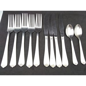 May include: A set of silverware, including forks, knives, and spoons, all made of polished stainless steel. The silverware has a simple, elegant design with a scalloped edge.