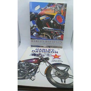 Könnte beinhalten: Zwei Bücher über Harley-Davidson-Motorräder. Das obere Buch trägt den Titel "Harley-Davidson The Complete History" mit einem Nahaufbild einer Motorrad. Das untere Buch trägt den Titel "The Gatefold Book of Harley-Davidson" mit einem Motorradbild und einem roten Stern.