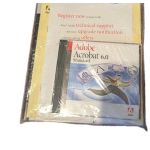 May include: A sealed package containing Adobe Acrobat 6.0 Standard software. The cover art features a running man with a red tie, a globe, and various computer-related icons. The package also includes promotional materials with the text "Register now to start it all".