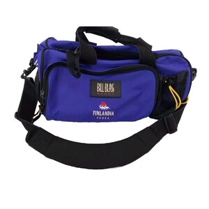 Puede incluir: Una bolsa de lona azul y negra con una correa de hombro negra. La bolsa tiene un logotipo blanco que dice "Bill Blass Sport" y "Finlandia Vodka".