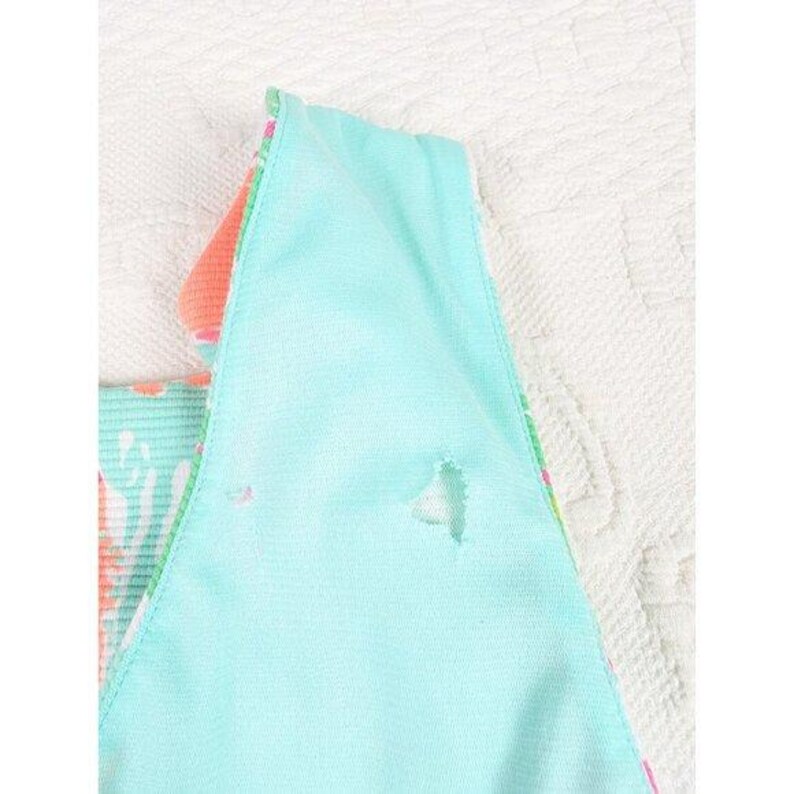 May include: Close-up of a section of a light blue garment with a hole. The garment has a floral pattern in shades of pink, green, and white. The edges are trimmed with a colorful floral print. The fabric appears to be soft and lightweight.