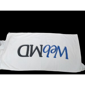 May include: White beach towel with the text "99.9 FM" in blue and gray lettering.