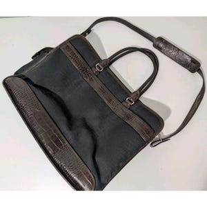 May include: A black leather briefcase with a brown crocodile embossed trim. The briefcase has a top handle and a shoulder strap.