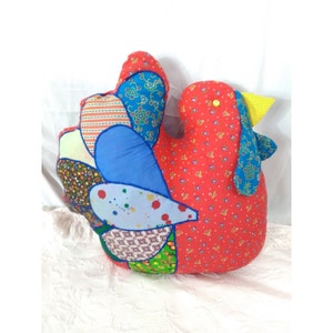 May include: A red, blue, green, and yellow patchwork fabric chicken pillow. The chicken has a yellow beak and a blue wing.